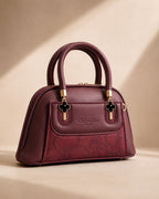 Burgundy wine maroon mini dome bowling bag for women with floral emboss detail gold hardware and black clover charm top handle luxury style 2026